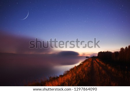 Waxing Crescent Moon above misty river scenery.