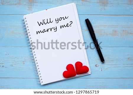 YOU WILL MARRY ME? word on notebook and pen with couple red heart shape decoration on blue wooden table background. Wedding, Romantic and Valentine’ s day concept