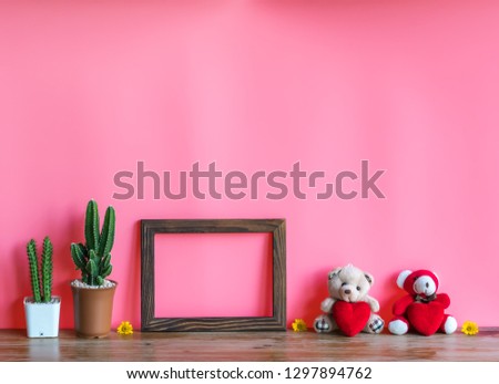 Valentine  concept  setting  with  two  teddy  bears  holding  red  heart,wooden  picture  frame  and  cactus  on  wooden  table  with  pink  background