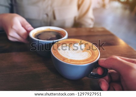 Close up image of a man and a woman clinking blue coffee mugs on wooden table in cafe