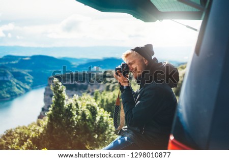 hipster tourist hold in hands taking photography click on retro vintage photo camera in auto, photographer looking on camera technology, panoramic landscape vacation concept, sun flare mountain