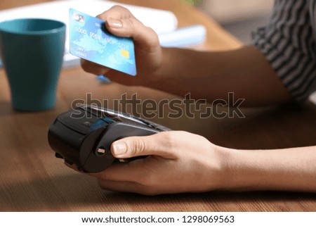 Woman using modern payment terminal at table indoors, closeup