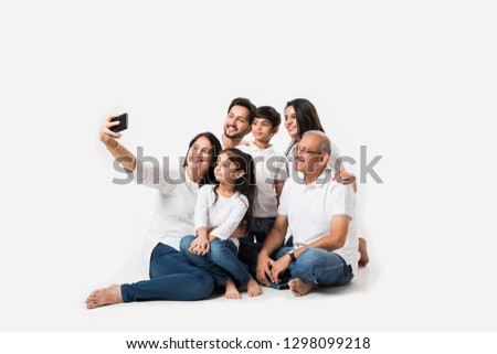Indian family taking selfie picture with smartphone while sitting on white background includes 3 generations. selective focus