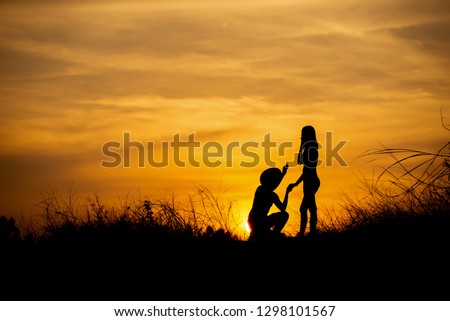 Silhouette of Couple of loves behind the sunset,man propose marriage to girlfriend,he kissed her hand.Lover and Valentine day concept.