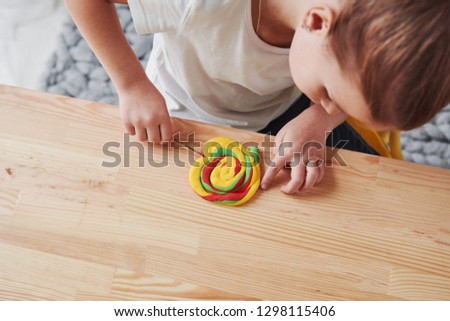 Making corrections to hand crafted artificial candy. Children playing with colored plasticine on the wooden table at home.