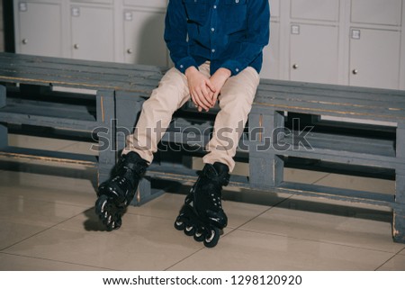 Partial shot of boy in black roller skates sitting on bench