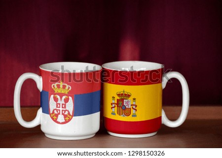 Spain and Serbia flag on two cups with blurry background