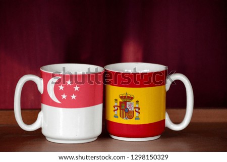 Spain and Singapore flag on two cups with blurry background