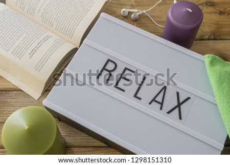 Text "relax"  written on white slate with book, candle, music and blanket on wooden background. Suitable for advertising