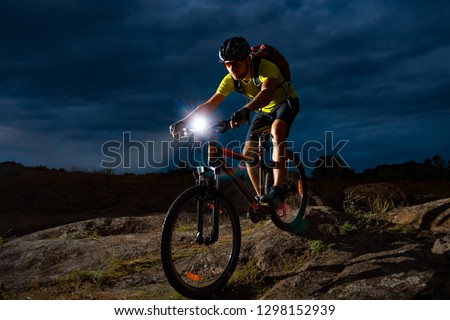 Cyclist Riding the Mountain Bike on the Rocky Trail at Night. Extreme Sport and Enduro Biking Concept.