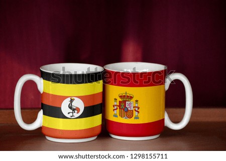 Spain and Uganda flag on two cups with blurry background