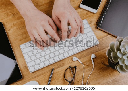 Top View of trendy wooden Office Desk with keyboard, white earphones and office supplies, working mans hands