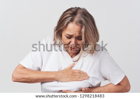 an elderly woman in a white T-shirt touches her breasts with her hands                   