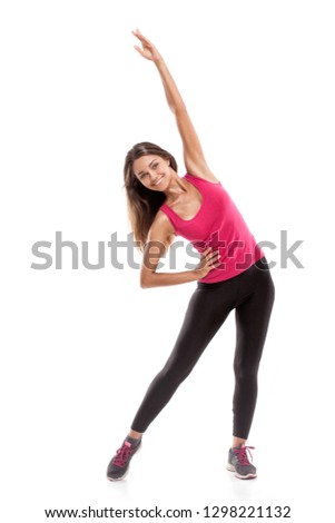 Studio shot of fitness woman doing stretching workout. Full length shot of young woman wearing pink shirt and black pants isolated on white background.