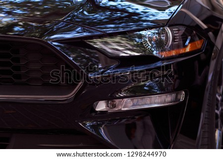 Close-up of front headlights, grill and hood of a new black modern car. Details of luxury cars.