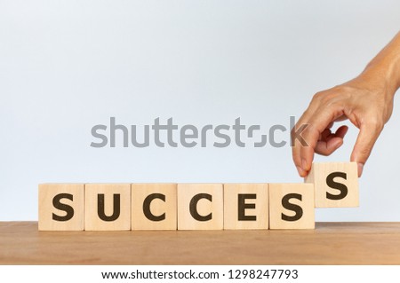 Hand arranging wooden cube with word SUCCESS on white background. Concept of achieving a goal. Success, leader and winner concept