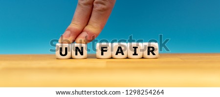 Dice form the word "UNFAIR" while two fingers push the letters "UN" away in order to change the word to "FAIR". Royalty-Free Stock Photo #1298254264