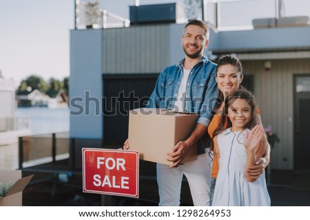 Positive young family standing with boxes near the house prepared for the removal