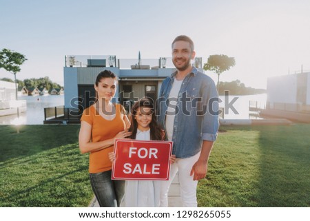 Positive nice smiling family holding a sign while standing near their house