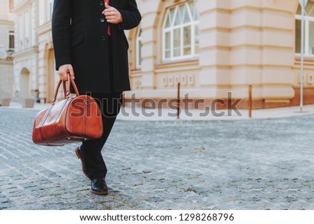 Focus on businessman in formal wear going along urban street. He is carrying elegant handbag. Copy space in right side
