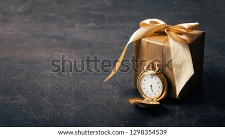 Gold pocket watch and craft paper gift with ribbon on dark background. Wedding, elegant, Love, romance, Valentines day concept.