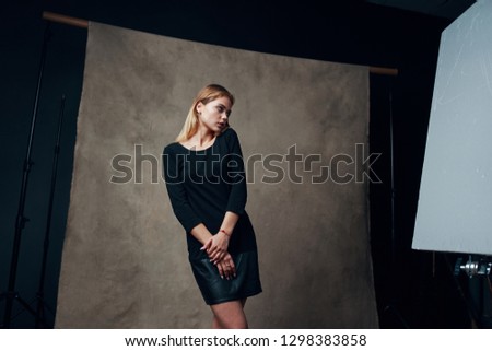 An embarrassed woman in a black dress holds her hands in front of her and looks away                          