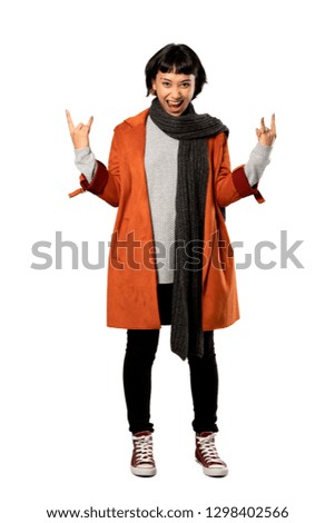 A full-length shot of a Short hair woman with coat making rock gesture over isolated white background