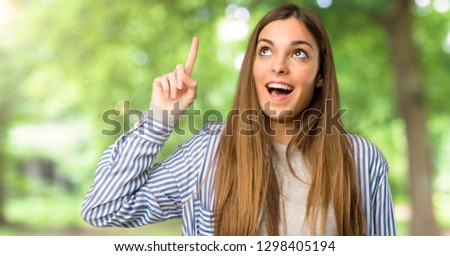 Young girl with striped shirt intending to realizes the solution while lifting a finger up at outdoors