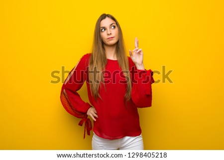 Young girl with red dress over yellow wall with fingers crossing and wishing the best