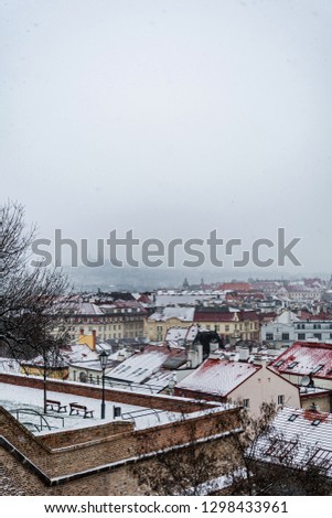 Roofs of Prague with a view point on a defensive wall covered snow in winter Prague Castle in fog in the background