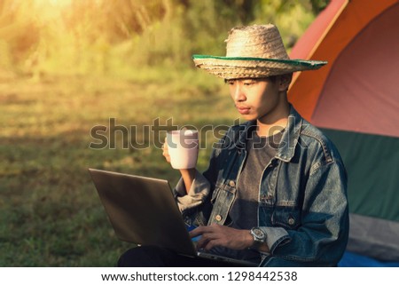 Young male student uses laptop while goes camping in forest, drink coffee in the morning in relaxing vacation holiday
