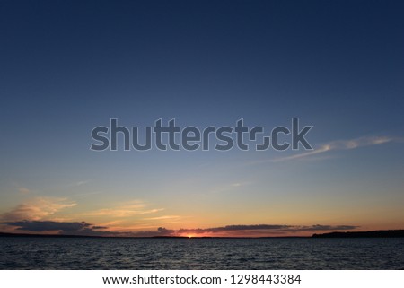 Sunset is a small bright point on the horizon the sun is infinite in space the blue of the sky and the water of the lake