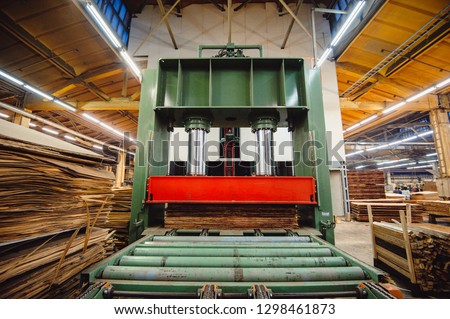 A large hydraulic press in the shop in the middle of the wood blanks presses the wood layers for the production of plywood. Workshop for the production of particle boards.  Wood processing. Royalty-Free Stock Photo #1298461873