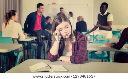 Portrait of unhappy girl sitting apart in class, having conflict with fellows students