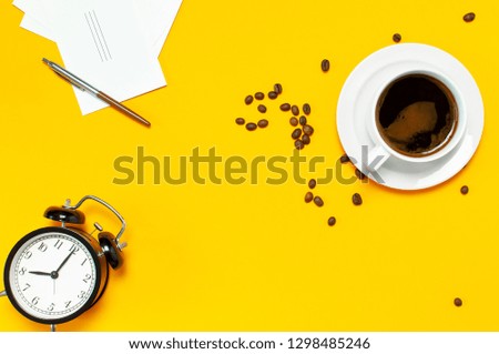 Flat lay cup black coffee, coffee beans, black alarm clock, pens, white cards on yellow background top view copy space. Creative Concept time to work, female desktop, coffee background