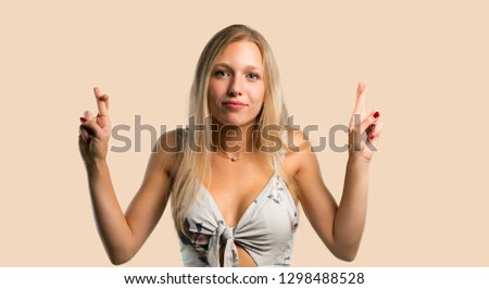 Young blonde woman with fingers crossing and wishing the best. Making a wish. on ocher background