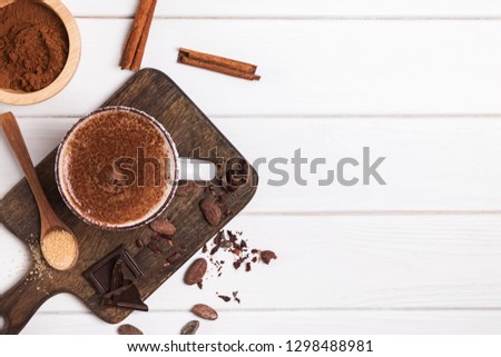 Hot chocolate in the cup, cocoa beans and powder on the white wooden table, top view