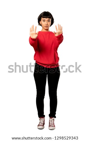 A full-length shot of a Short hair girl with red sweater making stop gesture and disappointed over isolated white background