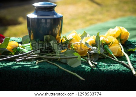 Ceramic burial urn with yellow roses, in a morning funeral scene, with space for text on the right Royalty-Free Stock Photo #1298533774