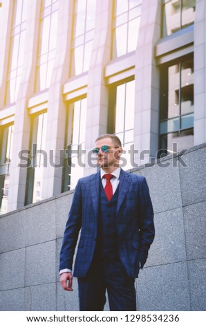 Serious business man in a fashionable stylish checkered suit on the background of a concrete gray business center (offices). Business life in the city. Portrait of a modern businessman