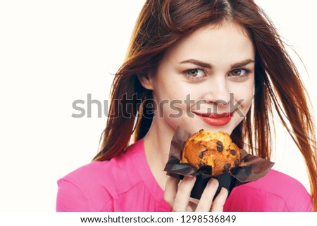 beautifully elegant woman in a pink blouse holding a cupcake in her hands near her face on bright background