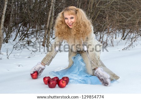 Smiling young woman with unusual hairstyle poses with apples in winter forest