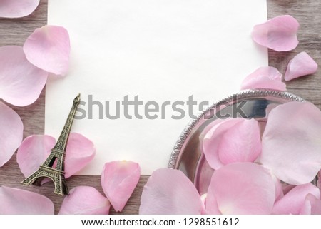 Romantic pink rose petals on vintage silver plate and an Eiffel Tower miniature on wooden background with white blank copy space for text for valentine's day card or wedding ceremony