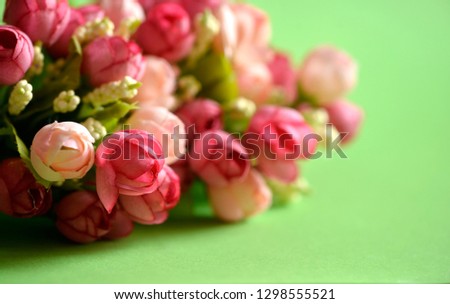 Pink vase with a bouquet of artificial flowers of roses on a light green background