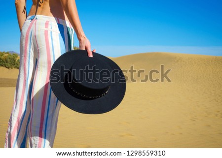 Woman holding a hat in her hand against the background of sand dunes and a blue sky. Close-up. Fashion. Summer rest.