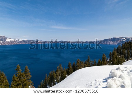 Deep and dark blue water in Crater Lake with contrasting white snow on the mountainous banks with blue sky in spring.
