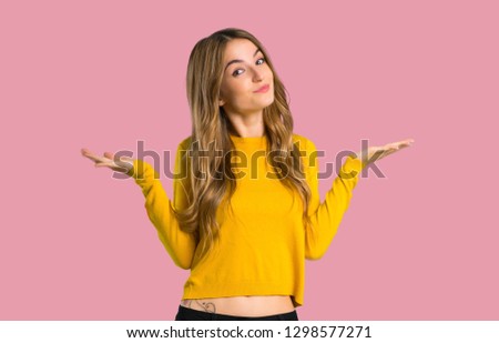 young girl with yellow sweater making unimportant gesture while lifting the shoulders on isolated pink background