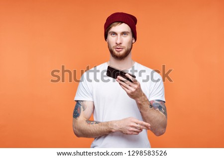 handsome man in a white T-shirt with tattoos on his hands on an orange isolated background with a phone in his hands