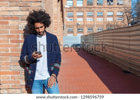 Portrait Young handsome African man using his smartphone with smile while leaning on a bricked wall outdoors in sunny day