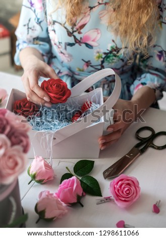 Flower shop: florist girl collects a bouquet of red roses in a blue paper basket.